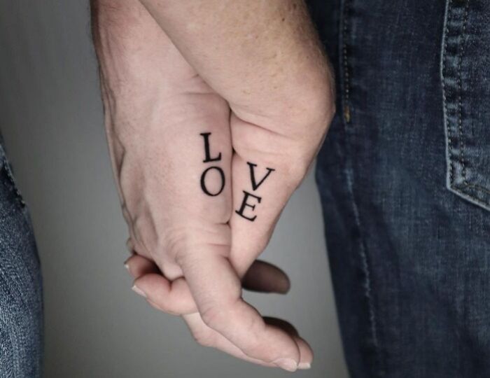 Matching tattoos spelling "LOVE" on a couple's fingers while holding hands, symbolizing connection and unity.