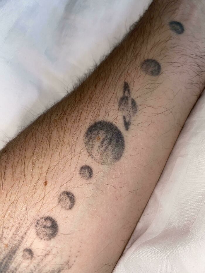 Arm with a solar system tattoo, matching a circular shadow perfectly with the tattooed planets.