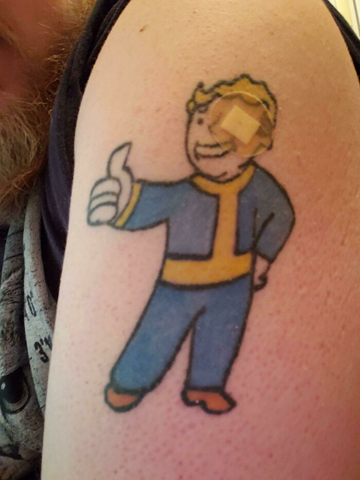 Tattoo of a cartoon character on a bicep, with a bandage over its eye, matching the situation humorously.