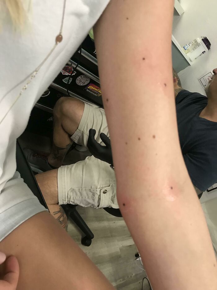 Tattoo matches freckles on arm in tattoo studio with artist in the background.