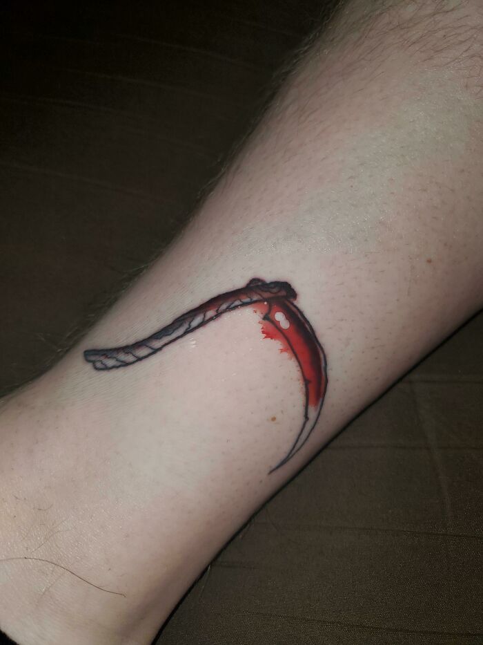 A tattoo of a scythe on a leg, perfectly aligning with a red scar for accidental matching effect.
