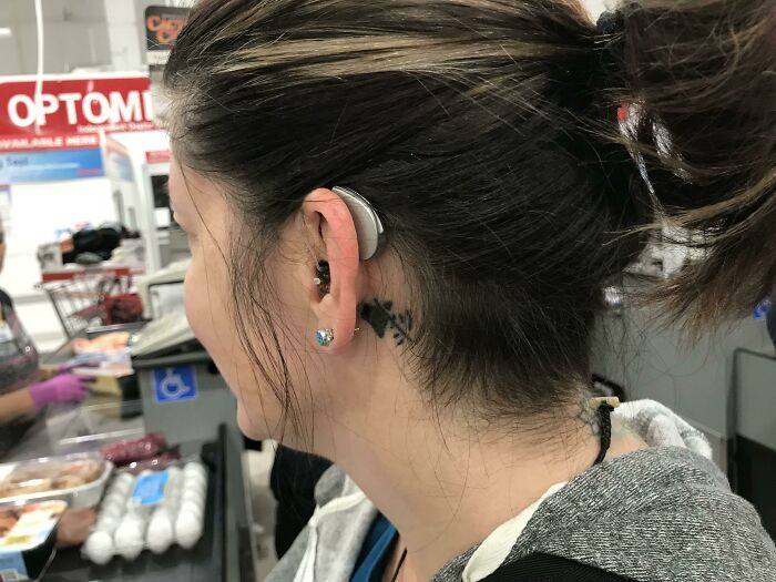 Person with a hearing aid and a matching tattoo behind the ear standing in a store.