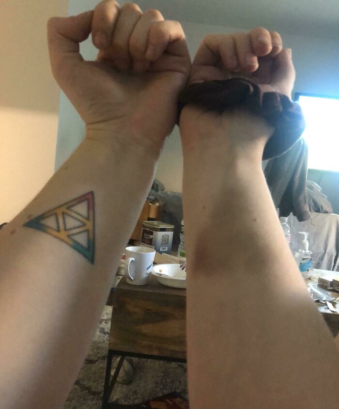 Tattoo of a colorful geometric triangle matches a wrist mark perfectly.