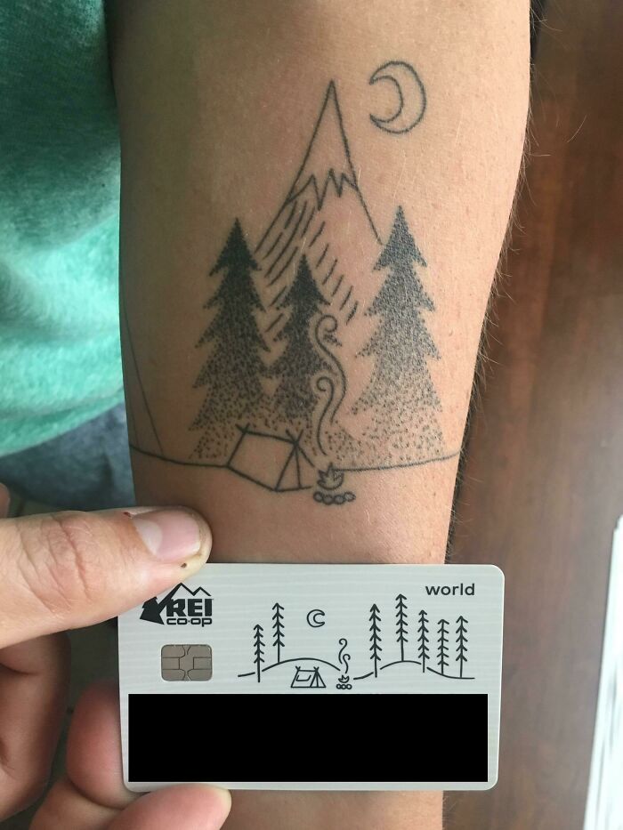 Tattoo of a camping scene on an arm perfectly matches the design on an REI card.