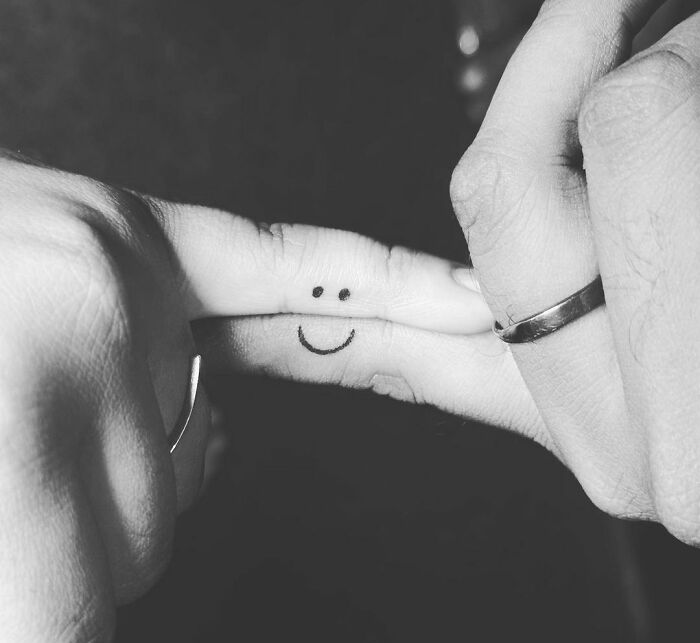 Two fingers with matching tattoos form a smiling face, symbolizing connection and togetherness.