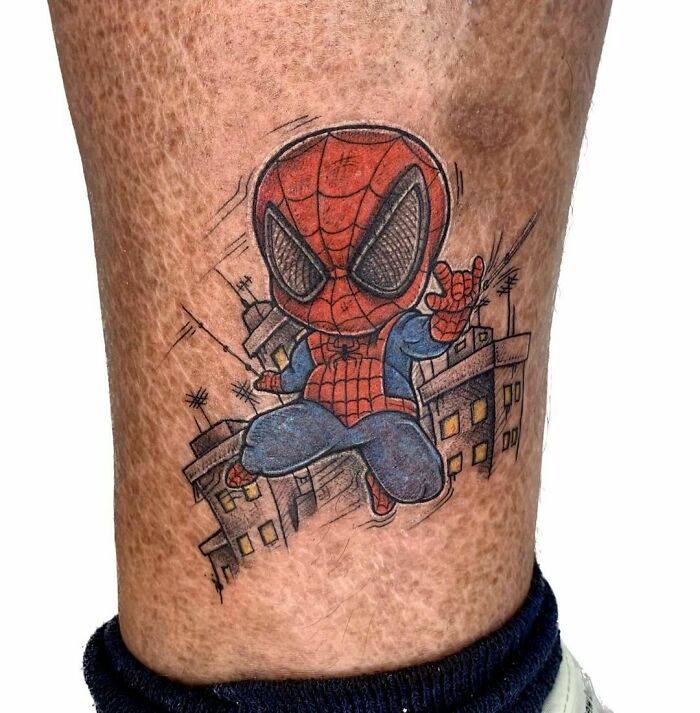 Marvel tattoo of Spider-Man in chibi style on leg, showcasing vibrant colors and cityscape background.