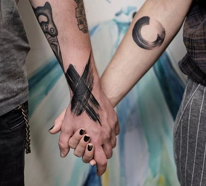 Couple holding hands with matching abstract tattoos, showcasing unique art and connection.