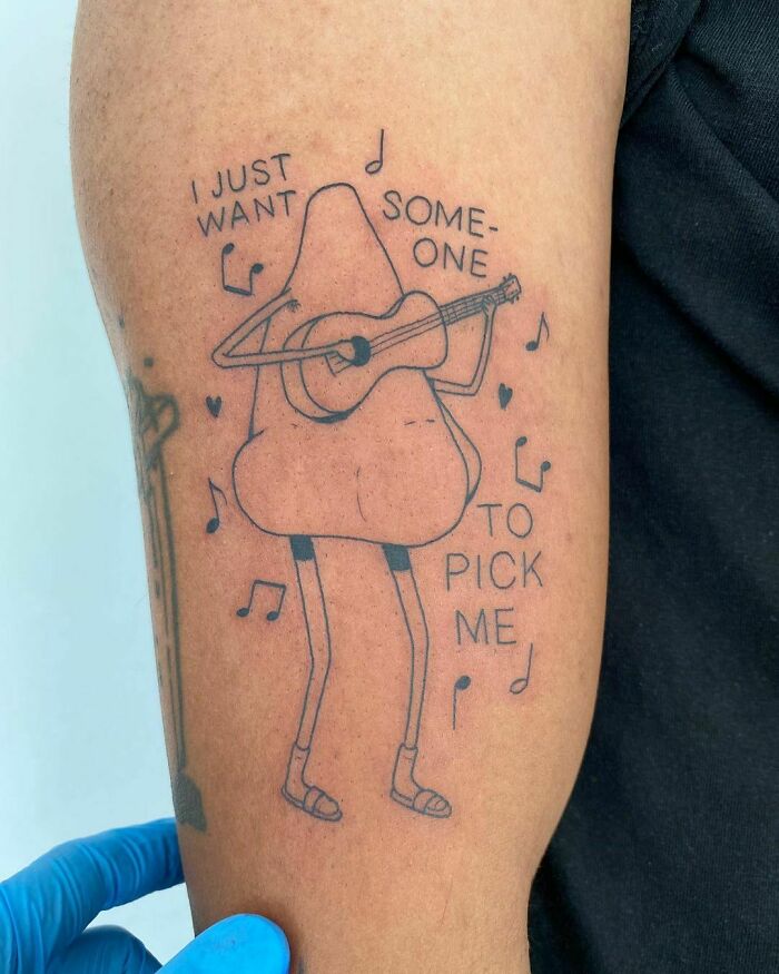 Quirky self-love tattoo with a guitar-playing nose, surrounded by musical notes, conveying humor and empowerment.