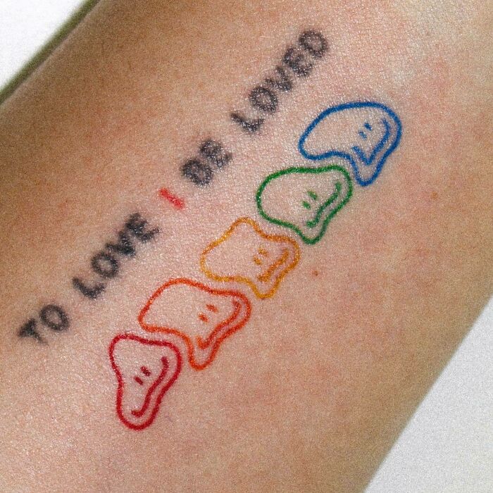 Self-love tattoo with "To love I be loved" phrase and colorful smiling shapes on skin.