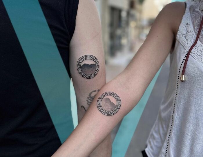 Matching tattoos on arms with circular Greek key design, symbolizing connection for special people in your life.