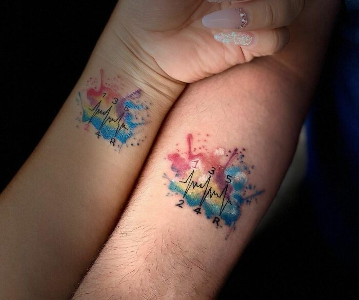 Colorful matching tattoos on arms, featuring heartbeats and numbers, symbolizing a special bond.
