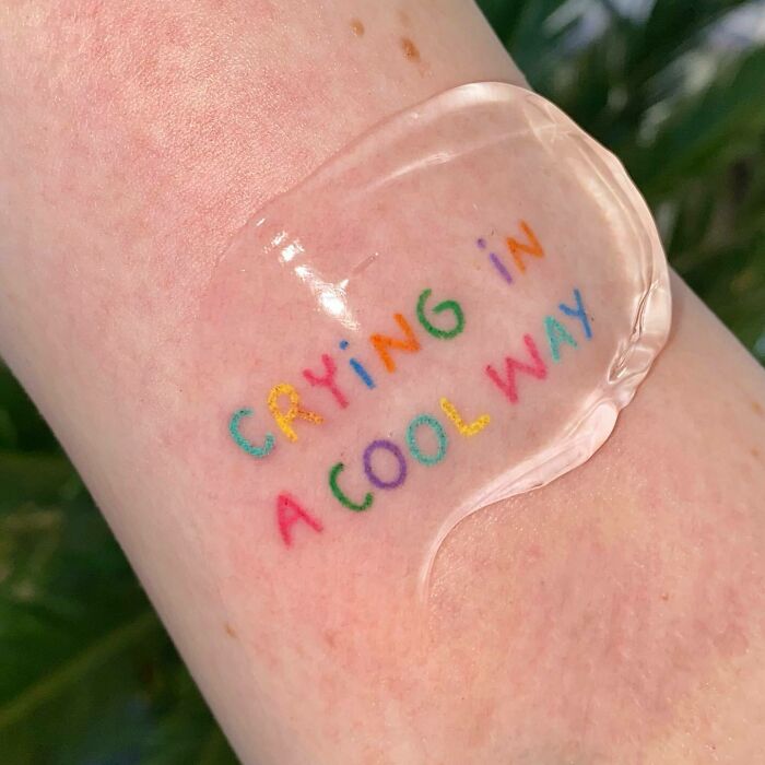 Colorful self-love tattoo on skin reading "Crying in a cool way," promoting empowerment and personal expression.