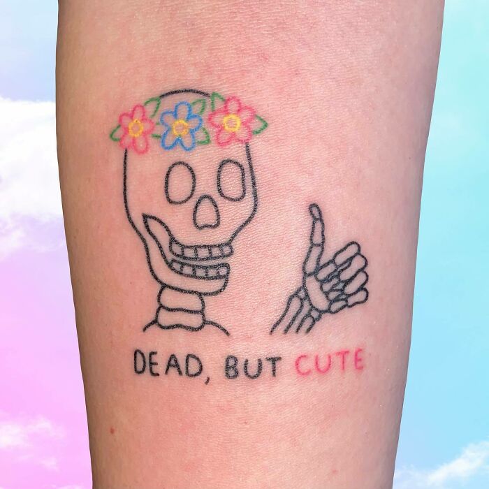 Self-love tattoo featuring a skeleton with a flower crown and "Dead, but cute" text on pale skin.