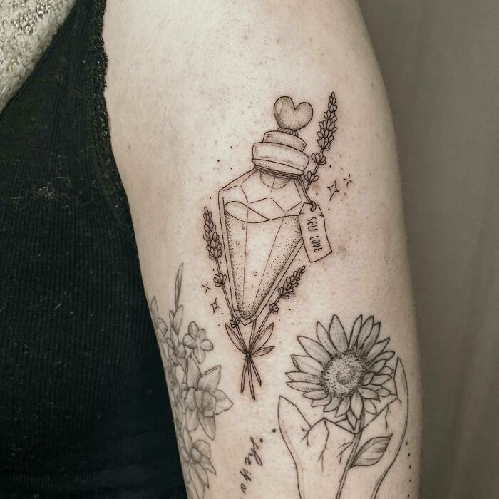 Self-love potion tattoo with flowers on arm, celebrating personal importance.