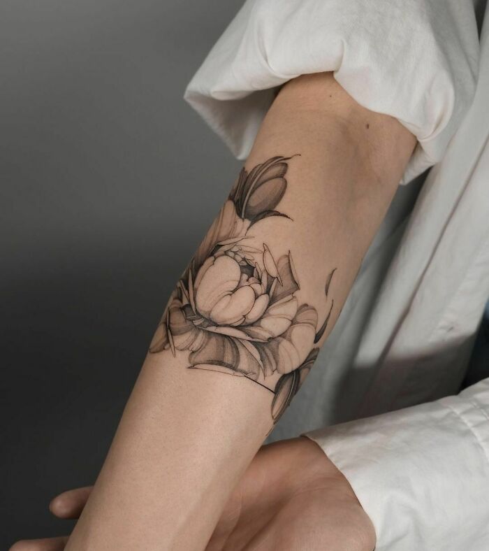 Flower tattoo on forearm, in black and gray, with detailed petals resembling natural blossoms.