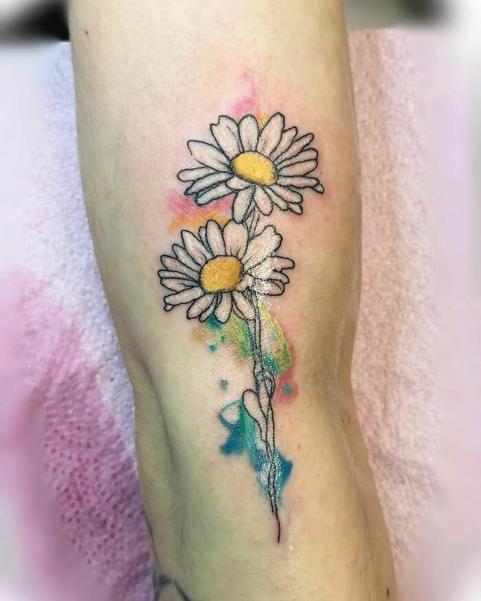 Flower tattoo of two daisies with colorful accents on forearm skin.