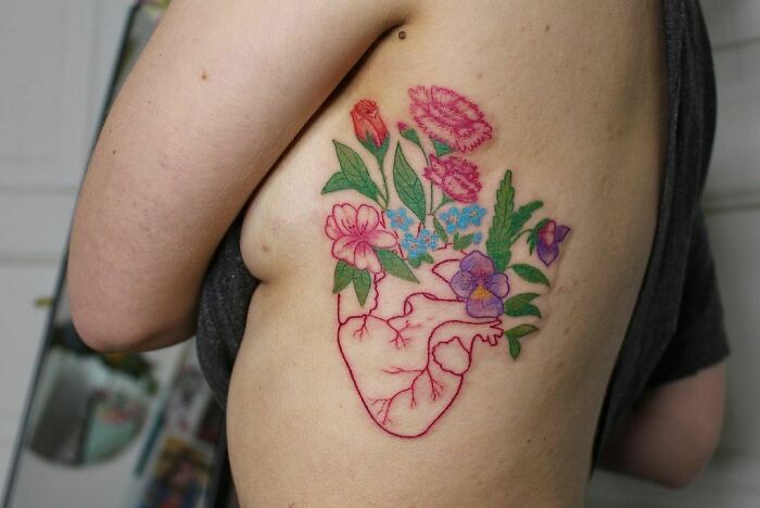 Self-love tattoo featuring a blooming heart with colorful flowers on a person's side.