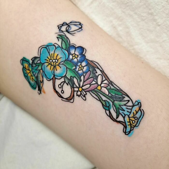 Colorful flower tattoo on arm with blue, yellow, and pink blossoms, showcasing vibrant floral art.