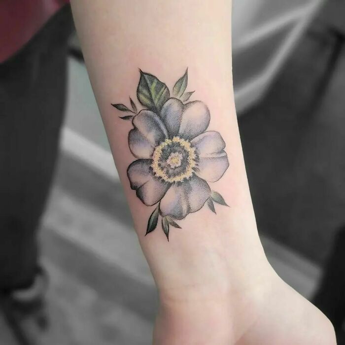 Flower tattoo on forearm, featuring detailed petals and leaves, appearing to blossom naturally on the skin.