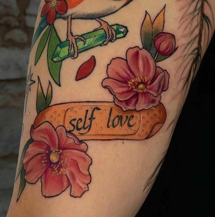Colorful tattoo with flowers, a bird, and a bandage featuring "self love" text.