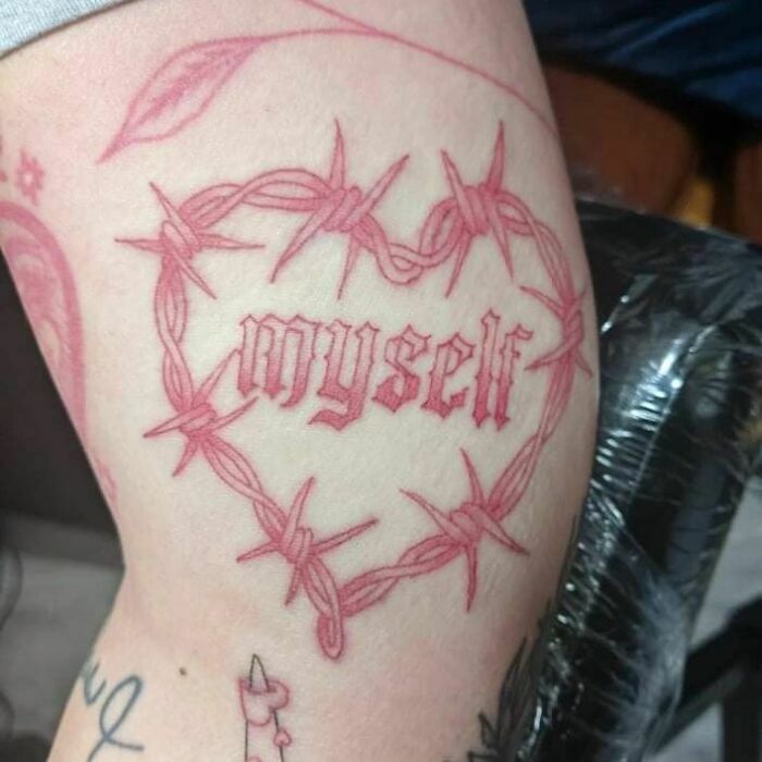 Tattoo of the word "myself" surrounded by a barbed wire heart, symbolizing self-love and empowerment.