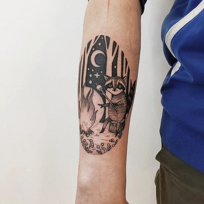 Animal tattoo of a raccoon by a campfire, blending simplicity and realism, on a person's forearm.
