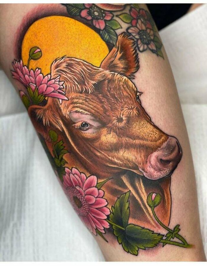 Realistic animal tattoo of a cow with pink flowers and a yellow background.