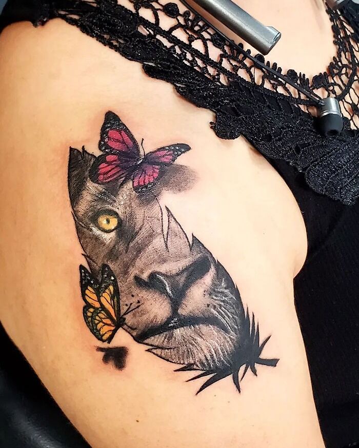 Lion tattoo with butterflies embracing simplicity and realism on upper arm.