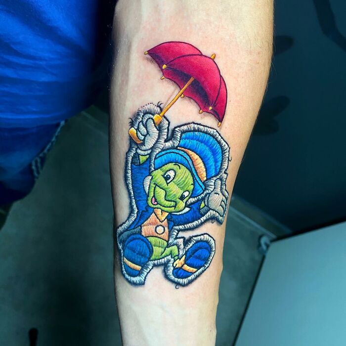 Tattoo featuring a vibrant cartoon character with an umbrella by Eduardo Lozano, showcasing a new dimension in tattooing.