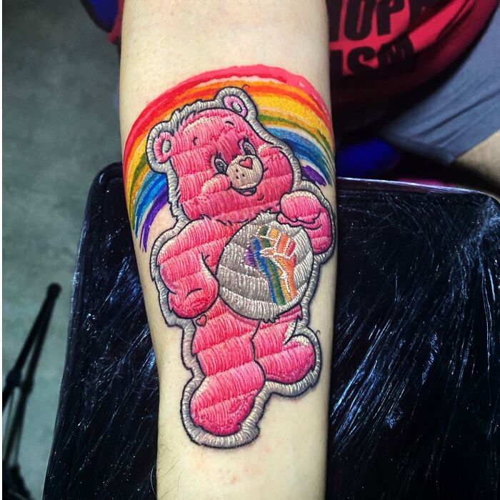 Tattoo of a pink bear with a rainbow on an arm, illustrating Eduardo Lozano's unique tattooing style.