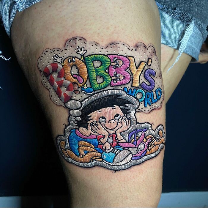 Tattoo by Eduardo Lozano featuring colorful "Bobby's World" design on a person's thigh.