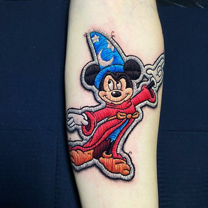 Embroidery-style tattoo by Eduardo Lozano featuring a famous cartoon character in a wizard outfit on an arm.