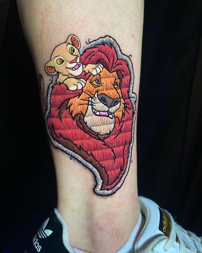 Tattoo of two animated lions by Eduardo Lozano, showcasing innovative embroidery style design on a person's leg.