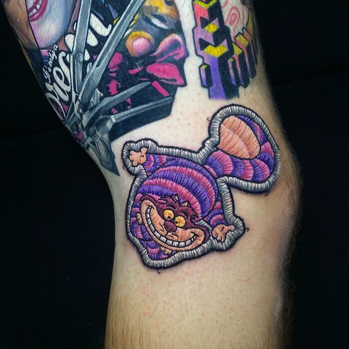 Intricate 3D tattoo of Cheshire Cat by Eduardo Lozano, showcasing unique embroidery style on skin.