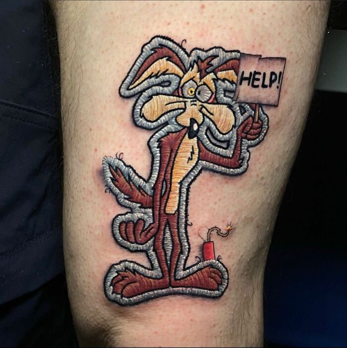 Tattoo of a cartoon coyote holding a "Help!" sign, illustrating Eduardo Lozano's unique style.