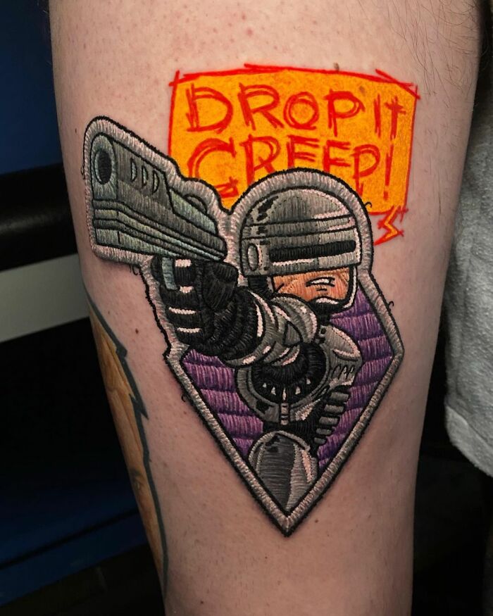 Tattoo of a futuristic soldier with a gun, by Eduardo Lozano, featuring bold colors and intricate embroidery-like details.