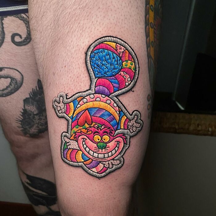 Colorful tattoo on a leg by Eduardo Lozano, featuring a vibrant, abstract Cheshire cat design.