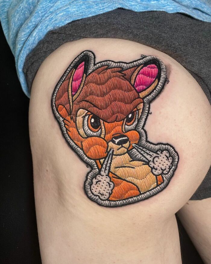 Tattoo by Eduardo Lozano featuring a cartoon animal with embroidery-style texture on a person's upper leg.