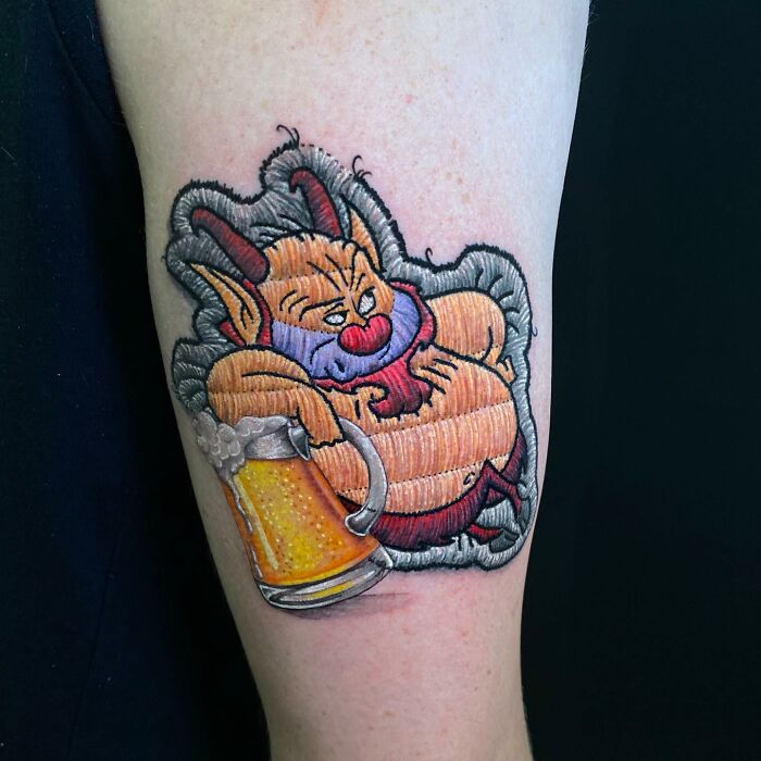 Tattoo by Eduardo Lozano depicting a cartoon character lounging with a beer mug, showcasing unique 3D embroidery style.