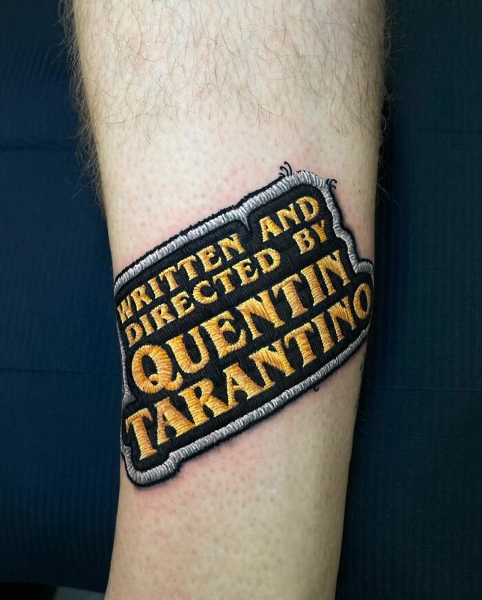 Tattoo on forearm reads "Written and Directed by Quentin Tarantino," showcasing Eduardo Lozano's tattooing style.