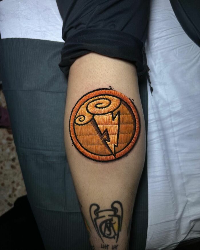 Tattoo on arm featuring an orange embroidered design, showcasing Eduardo Lozano's unique dimension in tattooing.