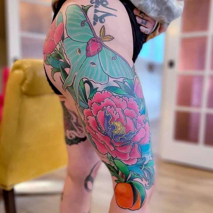 Colorful flower tattoo on thigh, featuring vibrant peonies and leaves, with detailed design.