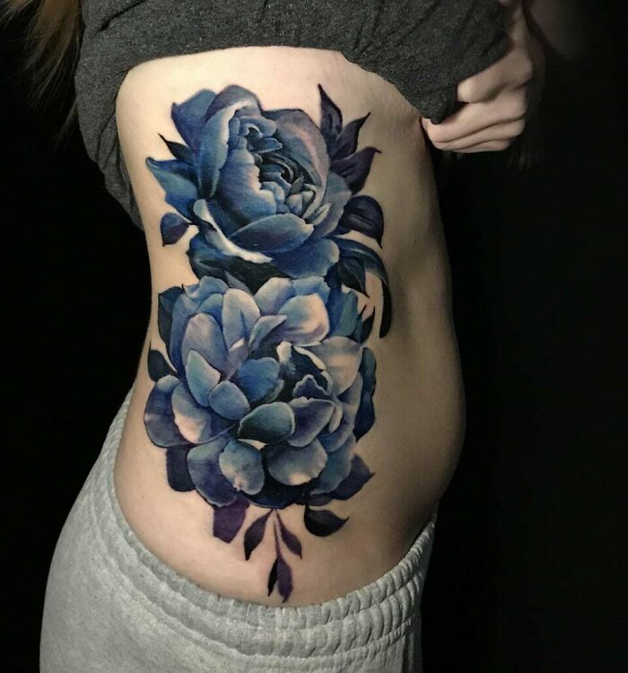 A vibrant blue flower tattoo adorning the side of a person, appearing to blossom on the skin.