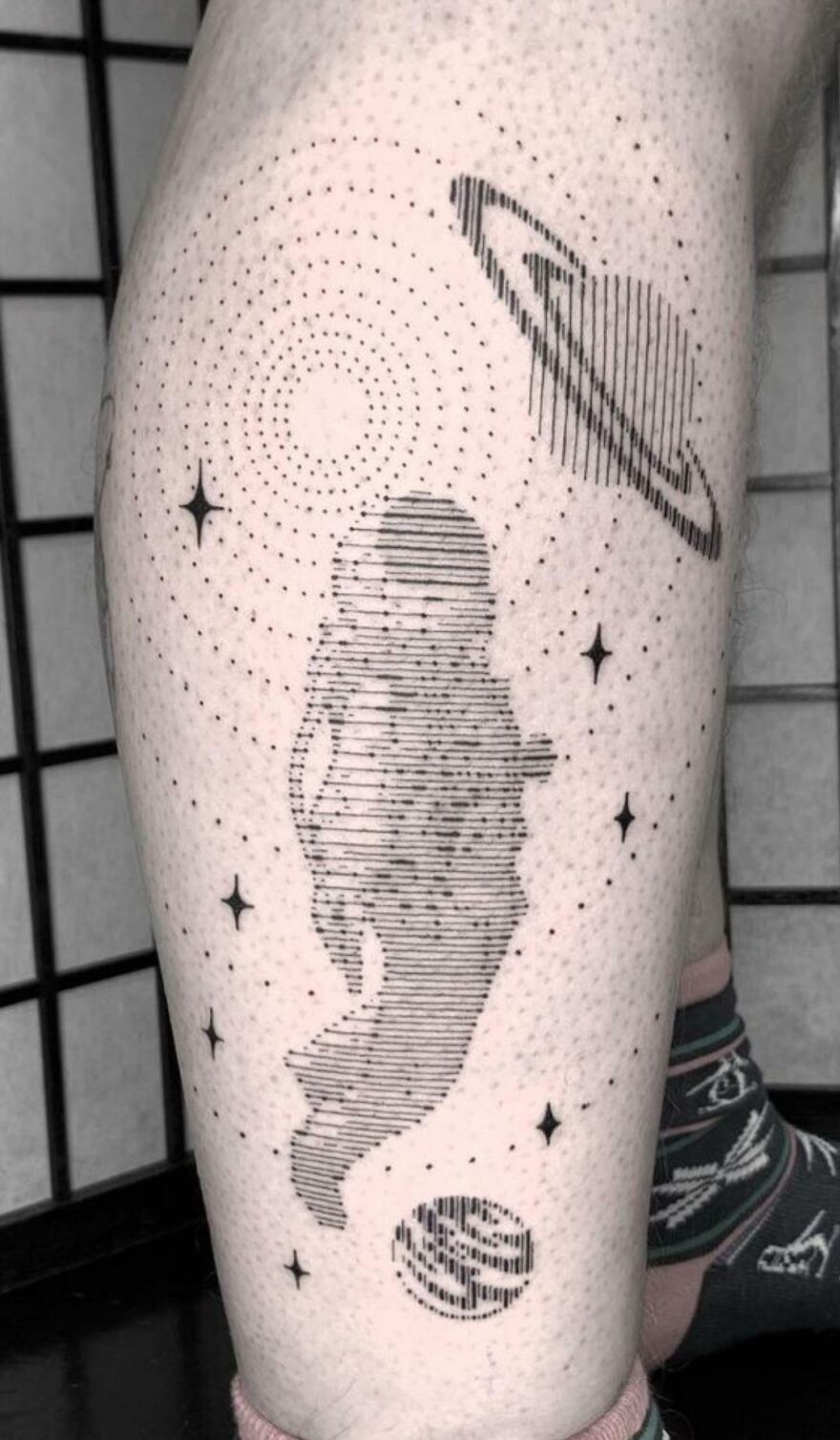 Space tattoo on leg featuring an astronaut, planets, and stars in a dotted design.