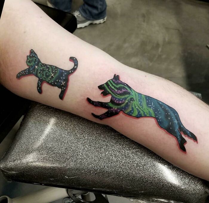 Space tattoos featuring a cosmic-themed cat and wolf with starry patterns on a forearm.