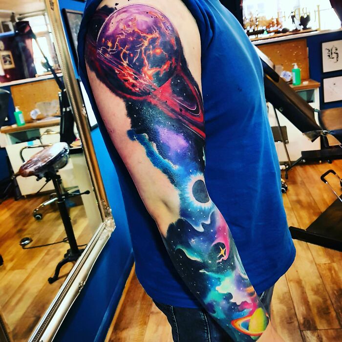 Colorful space tattoo sleeve featuring planets, nebulae, and cosmic elements in a tattoo studio setting.