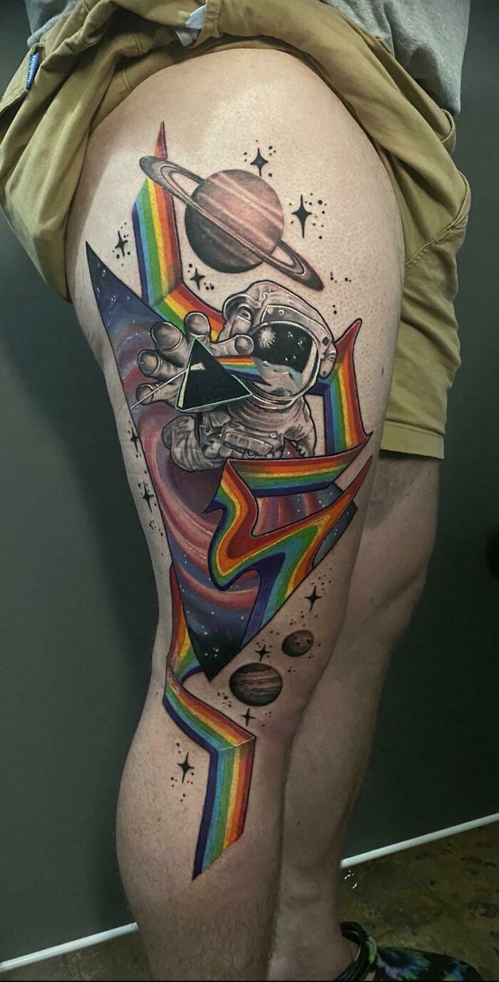 Astrology-themed space tattoo with an astronaut and planets on a person's thigh, featuring vibrant rainbow colors.