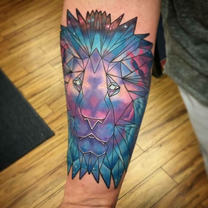 Geometric space tattoo of a lion with cosmic colors on a forearm.