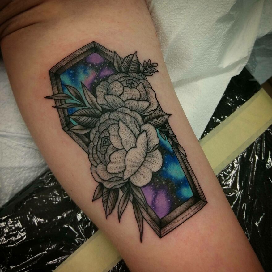 Space tattoo with floral elements and a colorful galaxy background on an arm.