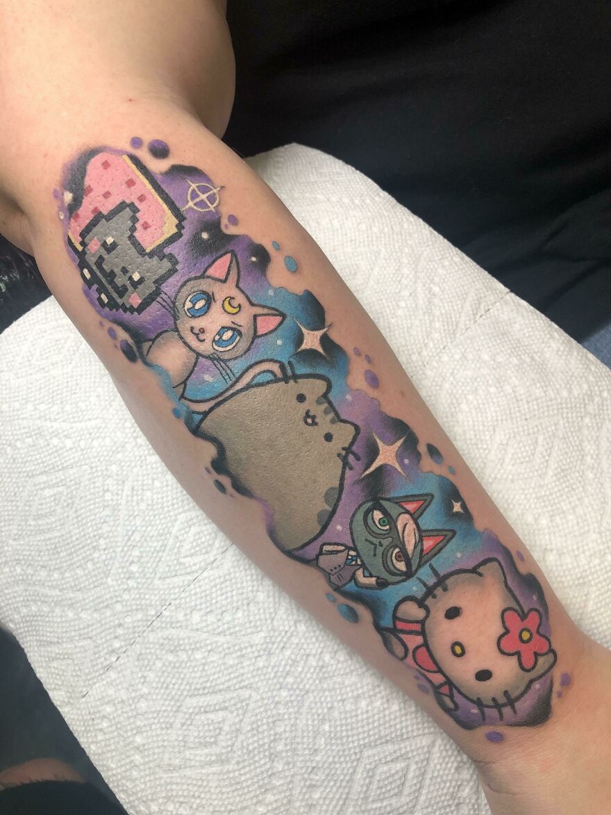 Colorful space tattoo featuring cartoon cats and cosmic elements on a forearm.